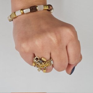 May include: A gold ring with a chain and multiple charms, including a small square, a circle, and a few other shapes. The ring is worn on a person's finger.