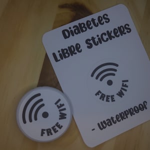 May include: White round sticker with a black Wi-Fi symbol and the text "FREE WIFI" in a circle. A white card with the text "Diabetes Libre Stickers - Waterproof" and a black Wi-Fi symbol with the text "FREE WIFI" in a circle.