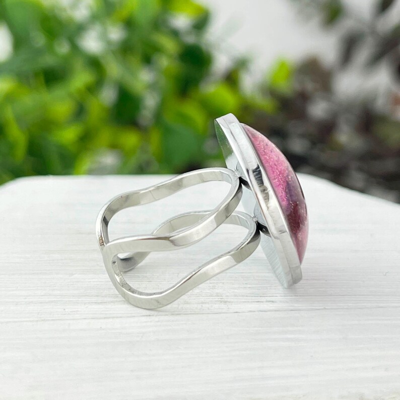 May include: A silver ring with a pink and black resin cabochon. The ring has a double band design.