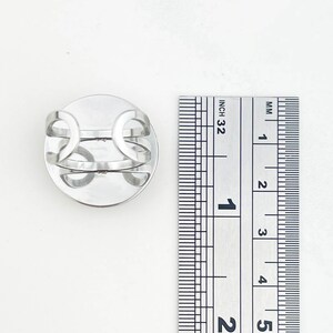 May include: Silver adjustable ring with a round, flat top. The ring is shown next to a ruler measuring 1 inch.