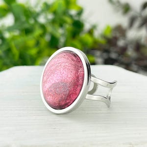 May include: A silver ring with a pink and white glittery round cabochon.