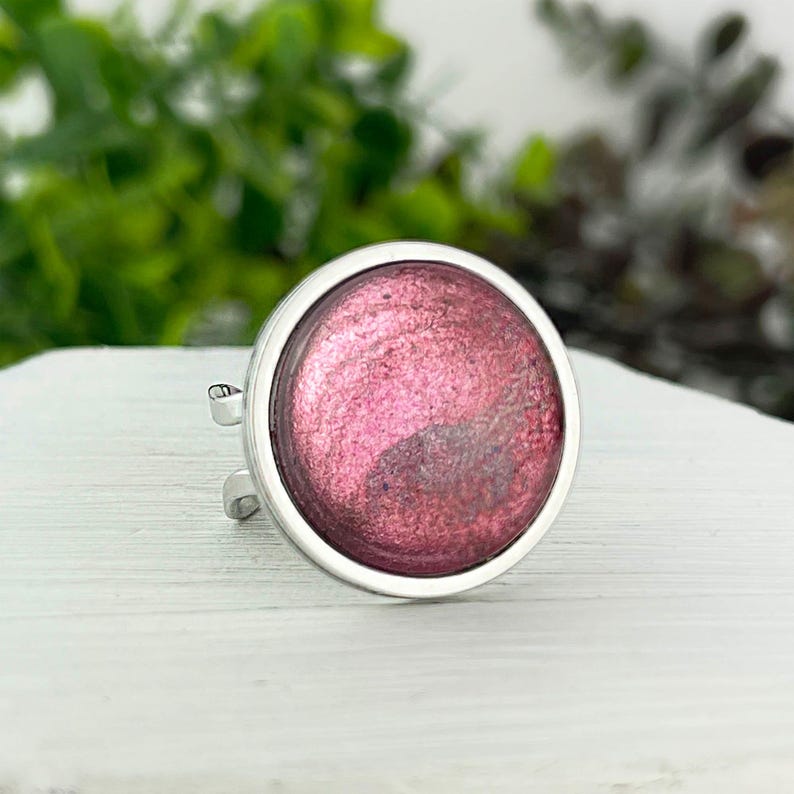 May include: A silver ring with a round, pink, glittery resin inlay.