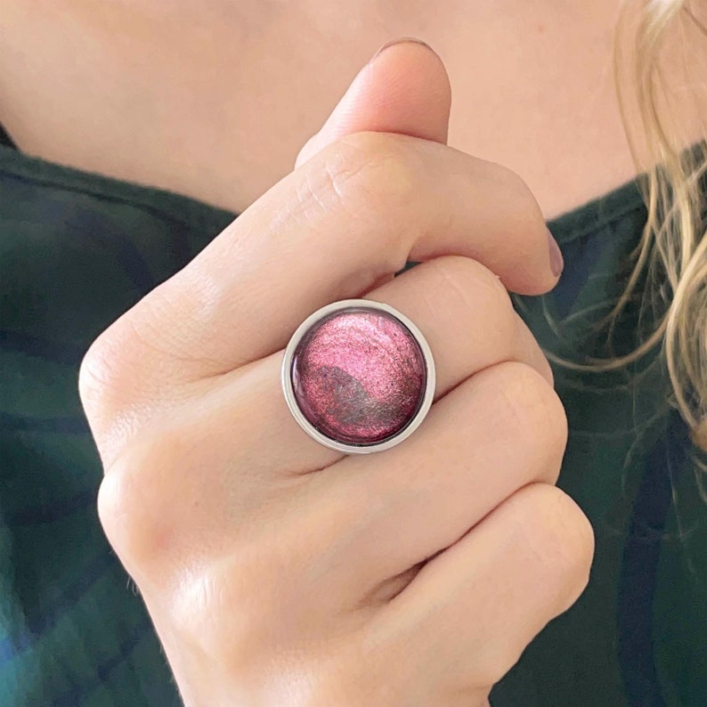 May include: A silver ring with a round, pink, glittery stone.