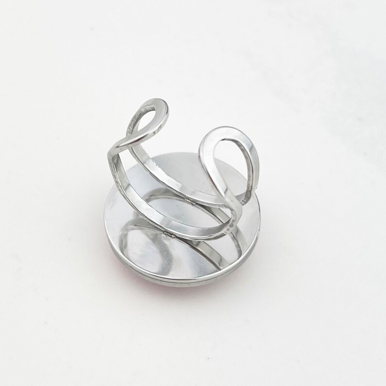 May include: Silver ring with a round, flat, silver base. The ring is adjustable and has a simple, modern design.