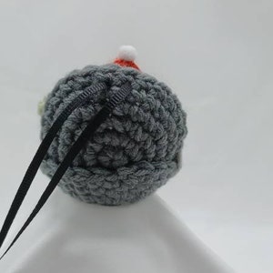 May include: A gray crocheted ornament with a red and white crocheted Santa hat. The ornament has a black ribbon attached to it.