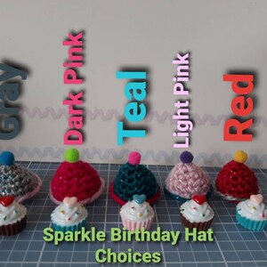 May include: Five crocheted cupcake hats in different colors: gray, dark pink, teal, light pink, and red. Each hat has a small pom-pom on top and a cupcake charm. The text "Sparkle Birthday Hat Choices" is below the hats.
