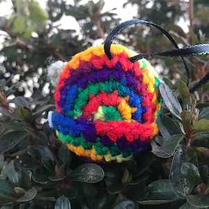 May include: A rainbow crocheted ornament with a black ribbon attached. The ornament is a spiral of colorful yarn.