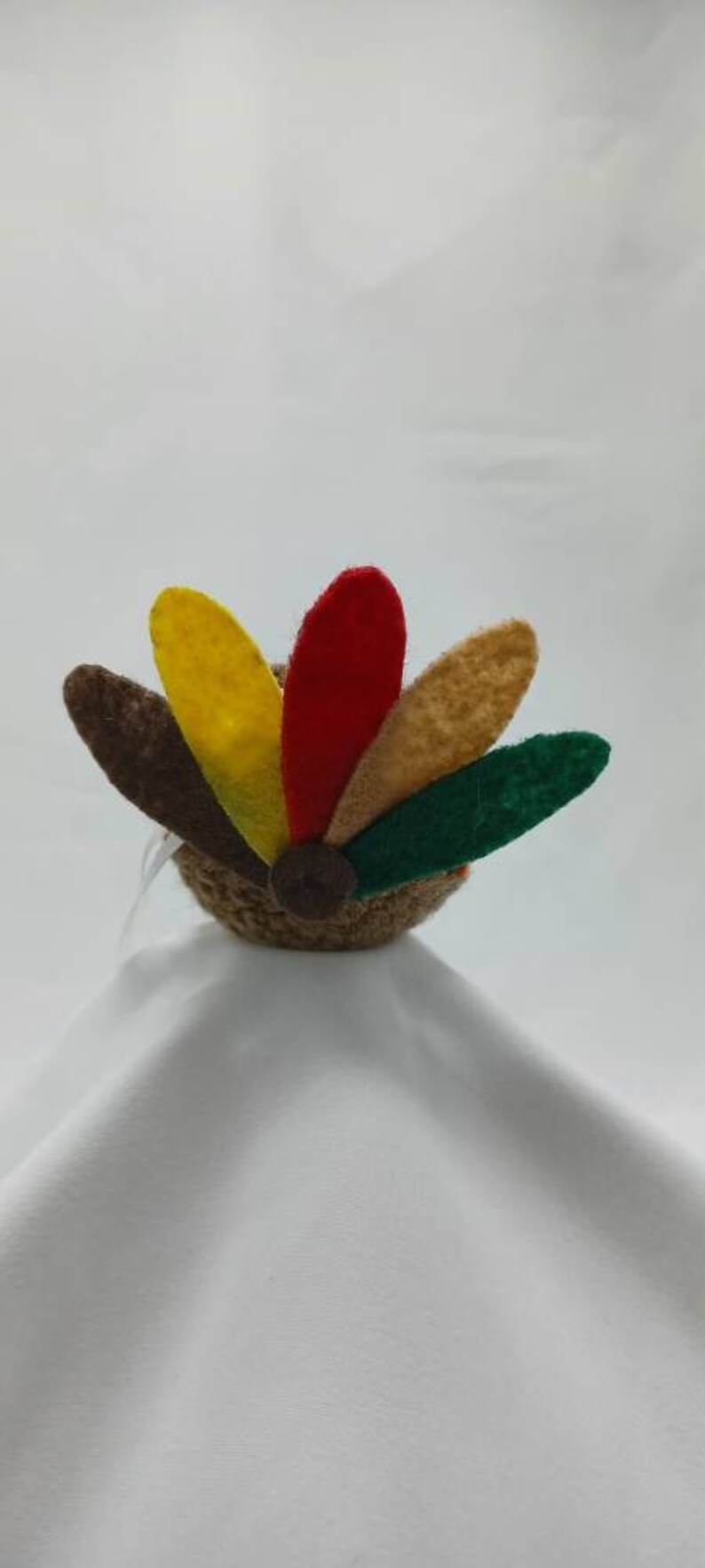 Puede incluir: Un pavo de fieltro marr&oacute;n con una cola de fieltro de colores. La cola tiene plumas rojas, amarillas, verdes y marrones.