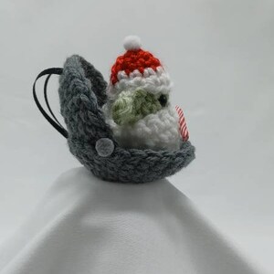 May include: A gray crocheted stocking with a white crocheted snowman wearing a red and white crocheted hat. The snowman is holding a red and white candy cane.