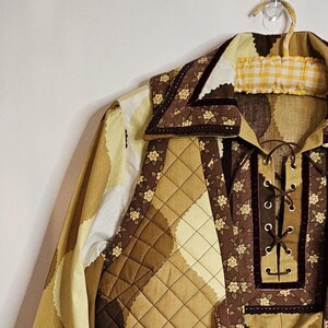 May include: A brown and yellow quilted shirt with a floral print and a lace-up front. The shirt has a large collar with a brown velvet trim.