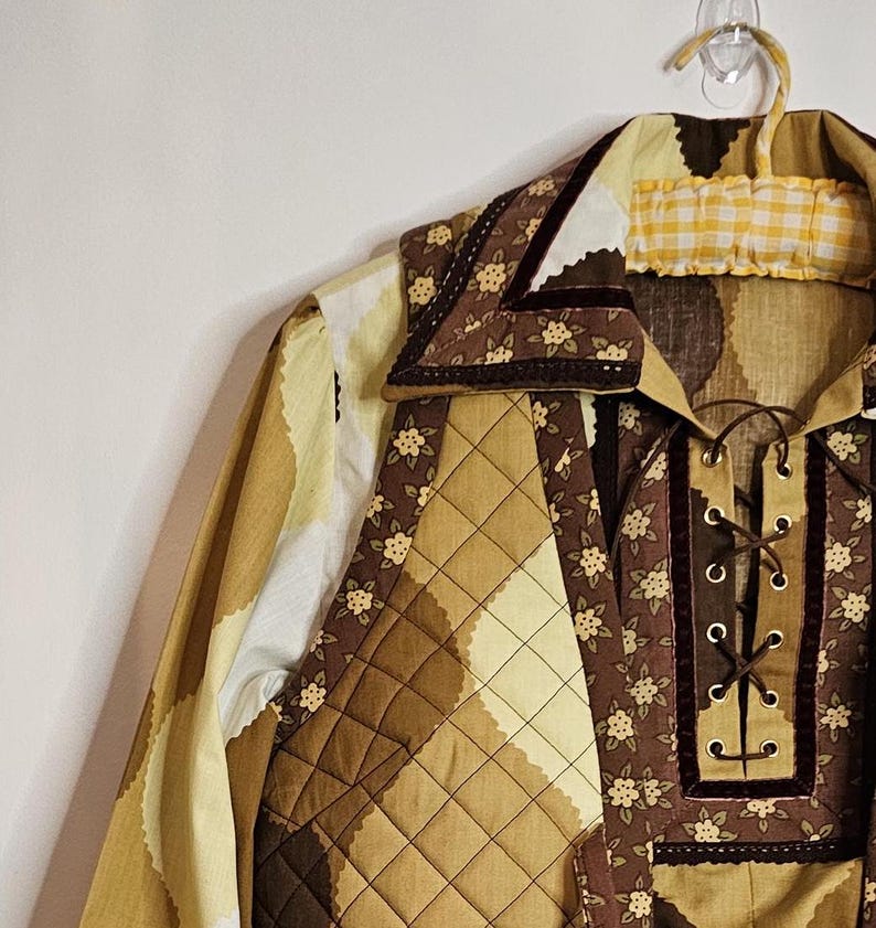 May include: A brown and yellow quilted shirt with a floral print and a lace-up front. The shirt has a large collar with a brown velvet trim.