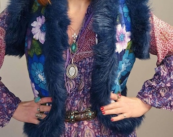 May include: A blue faux fur vest with floral embroidery and a purple paisley print dress. The vest has a wide collar and a brown belt with a metal buckle.