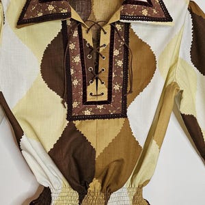 May include: A brown and cream patterned blouse with a lace-up neckline and a ruffled hem. The blouse has a brown velvet trim and a floral print.