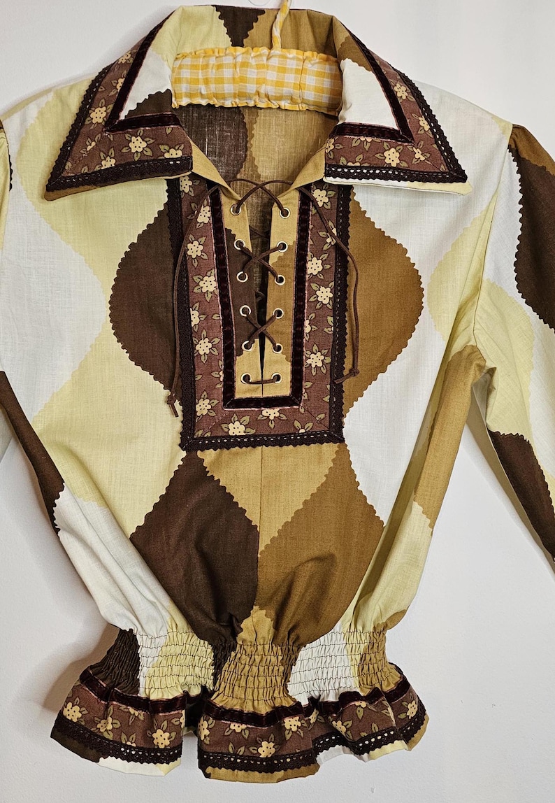 May include: A brown and cream patterned blouse with a lace-up neckline and a ruffled hem. The blouse has a brown velvet trim and a floral print.