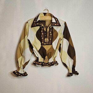May include: A brown and white patterned long-sleeved shirt with a lace-up neckline and a gathered elastic waistband. The shirt has a brown trim around the collar and cuffs.