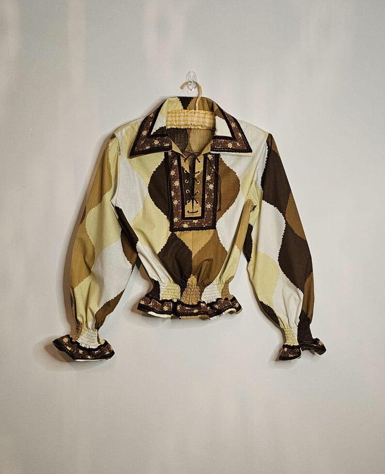 May include: A brown and white patterned long-sleeved shirt with a lace-up neckline and a gathered elastic waistband. The shirt has a brown trim around the collar and cuffs.