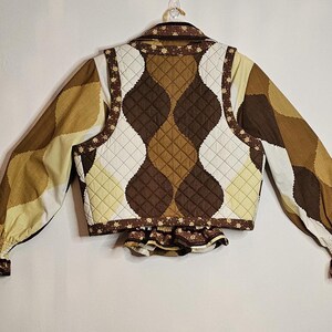 May include: A brown and white quilted vest with a floral print. The vest has a ruffled hem and long sleeves.