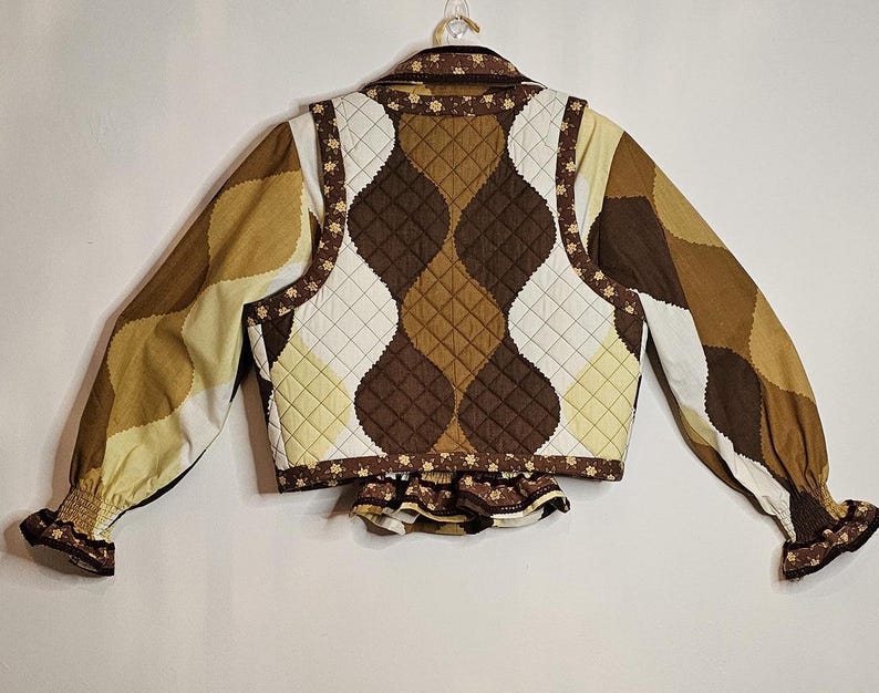 May include: A brown and white quilted vest with a floral print. The vest has a ruffled hem and long sleeves.