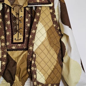 May include: A brown and cream quilted vest with a floral print and a matching brown and cream top with a lace-up neckline. The vest has a brown velvet trim and the top has a brown velvet ribbon.