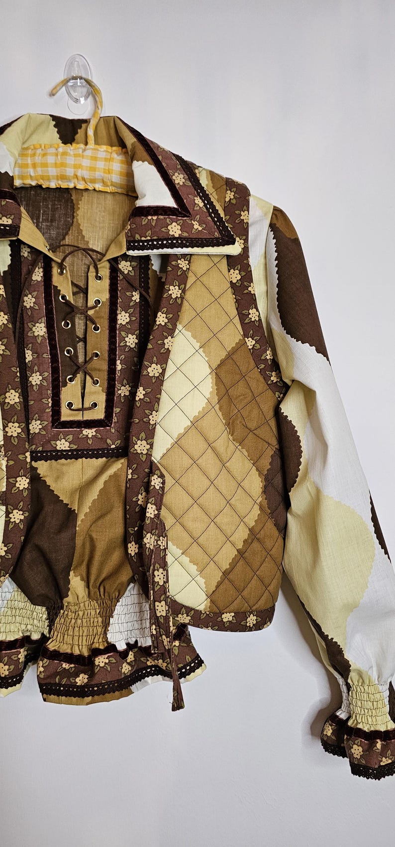 May include: A brown and cream quilted vest with a floral print and a matching brown and cream top with a lace-up neckline. The vest has a brown velvet trim and the top has a brown velvet ribbon.