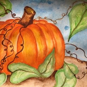 Puede incluir: Una pintura de acuarela de una calabaza naranja con hojas verdes y enredaderas marrones. La calabaza está sentada sobre una superficie marrón con un fondo azul.