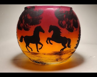 May include: A glass candle holder with a sunset gradient design. The holder features two black silhouettes of horses running across a field.