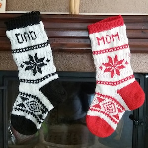 Può includere: Due calze di Natale a maglia, una bianca e nera con "DAD" e un motivo a fiocco di neve, e l'altra rossa e bianca con "MOM" e un motivo a fiocco di neve, appese al camino.