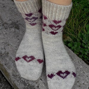 Può includere: Un paio di calzini di lana con base grigia e un motivo geometrico bordeaux. I calzini sono indossati sui piedi di una persona.