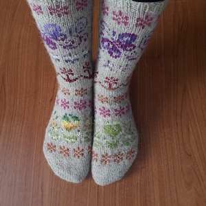 May include: A pair of knitted socks with a colourful floral pattern. The socks are beige with purple, green, yellow, and orange accents.