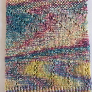 Può includere: Una sciarpa di maglia multicolore con un motivo traforato. La sciarpa è realizzata con una varietà di tonalità di blu, rosa, giallo e verde.