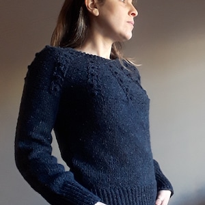 May include: A dark blue knitted sweater with a cable knit pattern around the neckline and shoulders.