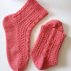 May include: A pair of coral pink knitted socks with a lacy pattern. The socks are made with a fine yarn and have a delicate, feminine look.