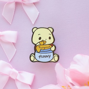 May include: A yellow cartoon bear wearing a blue shirt with the word "Hunny" on it. The bear is holding a pot of honey with a golden lid.