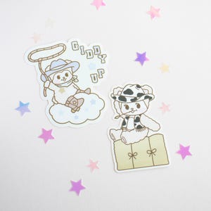 May include: Two adorable cartoon bear stickers with cowboy hats. One bear is holding a lasso and the other is sitting on a bale of hay. The stickers say "Giddy Up".