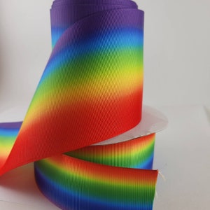 Può includere: Un rotolo di nastro ombré arcobaleno con finitura satinata. Il nastro è un degradé di viola, blu, verde, giallo, arancione e rosso.