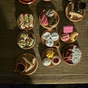Puede incluir: Una colección de platos de arcilla en miniatura con varios alimentos mexicanos, incluyendo tamales, pan dulce, churros y arroz. Los platos están dispuestos sobre una superficie de madera.