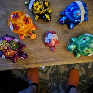 May include: Six colorful hand-painted turtle figurines with floral designs. The turtles are made of ceramic and have a glossy finish.