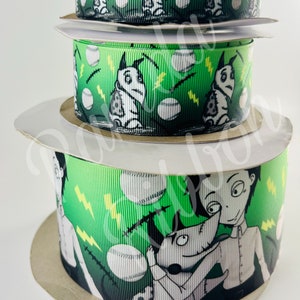 May include: Three rolls of green and black patterned ribbon with a white background. The pattern features a cartoon character with a stitched-up face and a baseball. The ribbon is on a white surface.