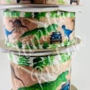Könnte beinhalten: Eine Rolle braunes, grünes und blaues Band mit einem Dinosaurier- und Jeep-Druck. Das Band zeigt ein sich wiederholendes Muster aus Dinosauriern, Jeeps und grünen Blättern.