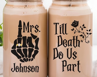 May include: Two clear glass tumblers with bamboo lids and metal straws, filled with a beige beverage. One glass features a black skeleton hand graphic with a gold ring, the text Mrs. Johnson, and the other says Till Death Do Us Part with a rose.