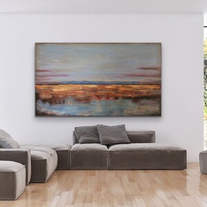 May include: Abstract landscape painting in shades of blue, orange, and brown, displayed above a modern sofa. The room has large windows and a minimalist design. The painting's dimensions are not visible. The sofa is a neutral colour.