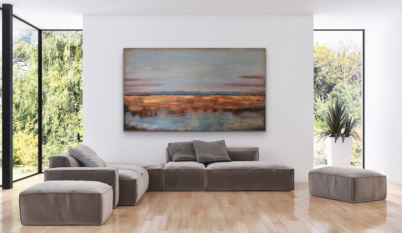 May include: Abstract landscape painting in shades of blue, orange, and brown, displayed above a modern sofa. The room has large windows and a minimalist design. The painting's dimensions are not visible. The sofa is a neutral colour.