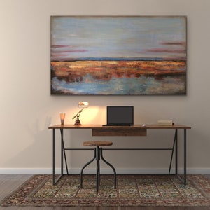 May include: A home office setup with a wooden desk, black laptop, small lamp, and stool. Above the desk hangs a large abstract painting with blue, orange, and brown tones. A patterned rug is on the floor.
