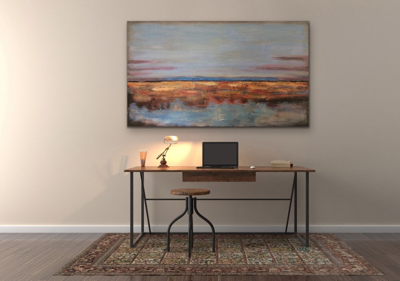 May include: A home office setup with a wooden desk, black laptop, small lamp, and stool. Above the desk hangs a large abstract painting with blue, orange, and brown tones. A patterned rug is on the floor.