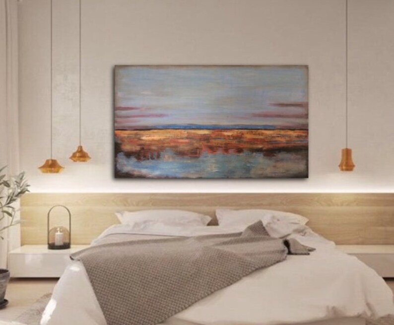May include: An abstract landscape painting in shades of blue, brown, and orange. The artwork shows a horizon line and its reflection in the water. The painting hangs above a bed with white bedding and a grey blanket. The artwork is a decorative piece.