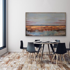 May include: An abstract landscape painting in shades of blue, orange, and brown hangs above a round dining table. The table is surrounded by six black chairs with wooden legs. The room has a large window and hardwood floors.