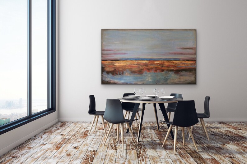 May include: An abstract landscape painting in shades of blue, orange, and brown hangs above a round dining table. The table is surrounded by six black chairs with wooden legs. The room has a large window and hardwood floors.