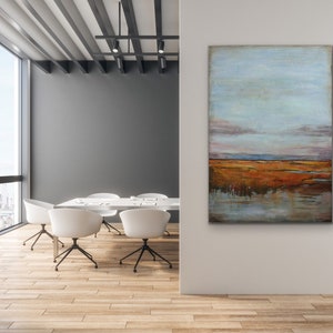 May include: Abstract landscape painting with a blue sky, orange and brown fields, and a reflection of the sky in the water. The painting is hanging on a white wall in a modern office setting.