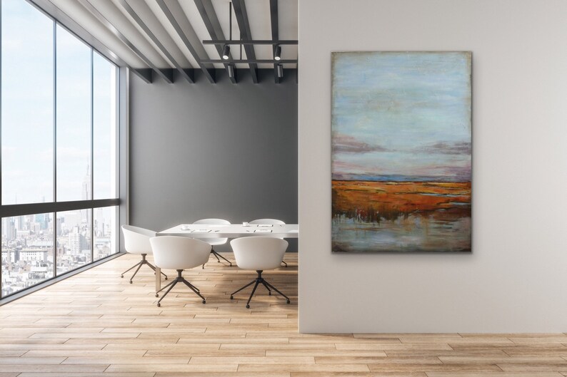 May include: Abstract landscape painting with a blue sky, orange and brown fields, and a reflection of the sky in the water. The painting is hanging on a white wall in a modern office setting.