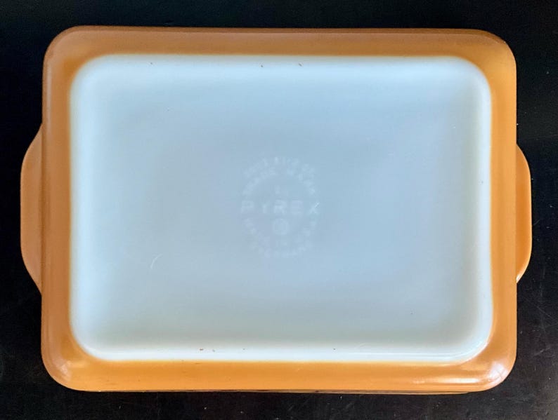 May include: Rectangular Pyrex baking dish with a light orange exterior and a white interior. The dish has rounded corners and small handles on each side. The Pyrex logo is visible in the center of the dish.